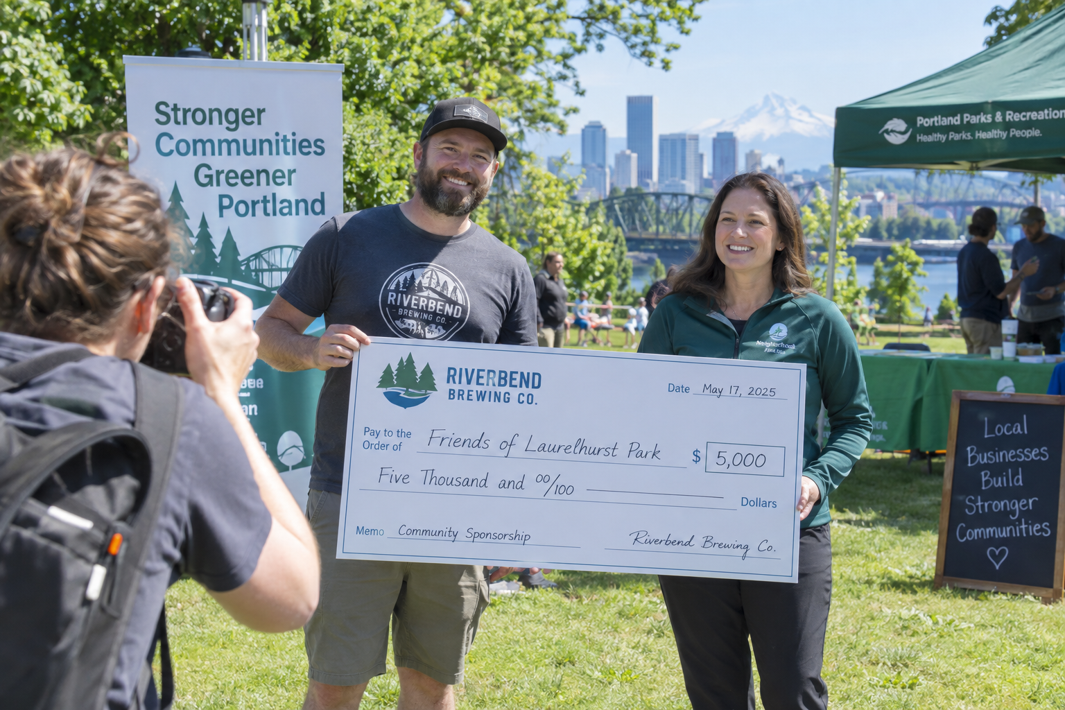Local business owner presenting a sponsorship check at a community event in a Portland park while a photographer captures the moment