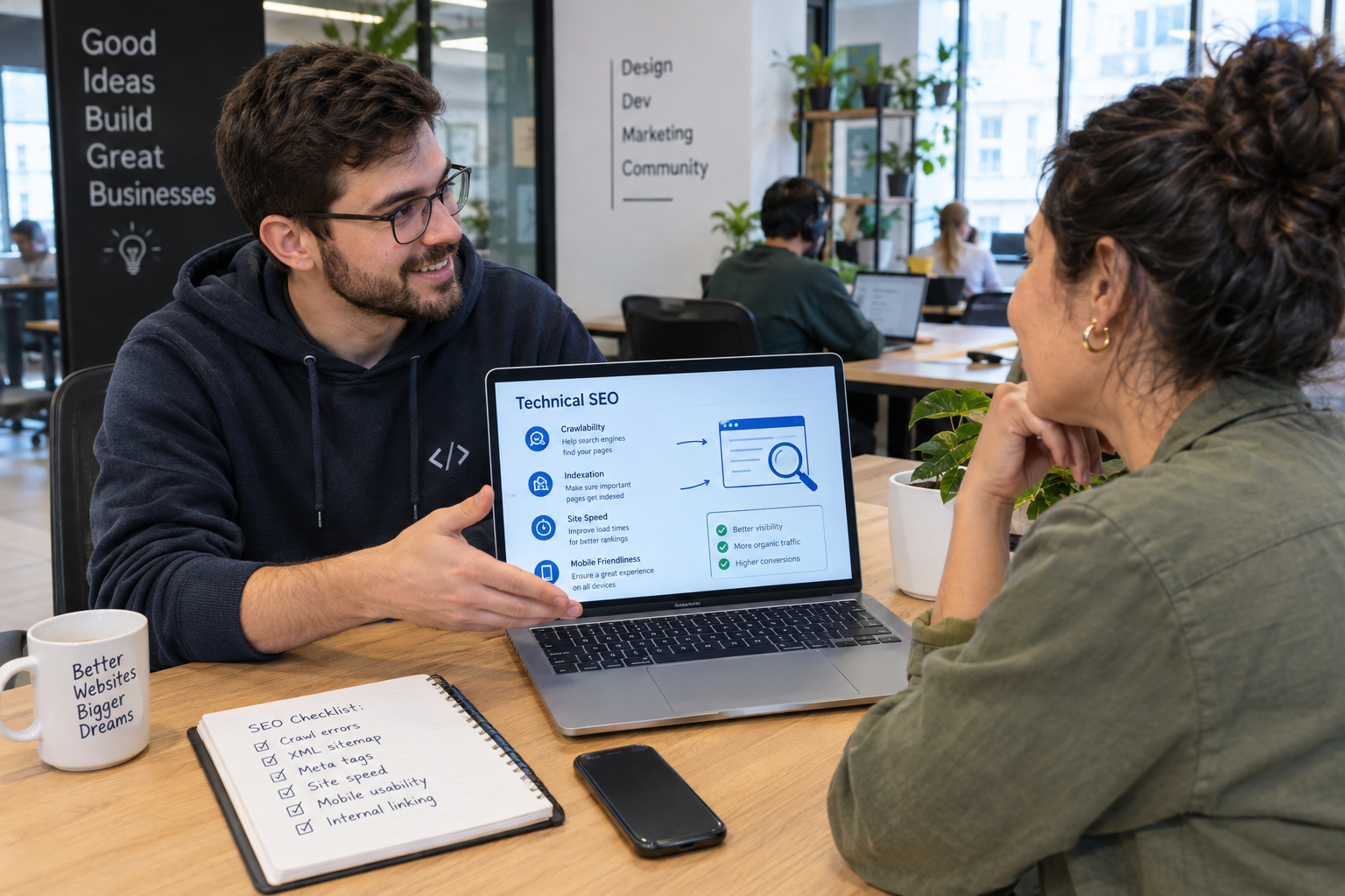 Web developer explaining technical SEO to a small business owner at a shared desk in a modern coworking space